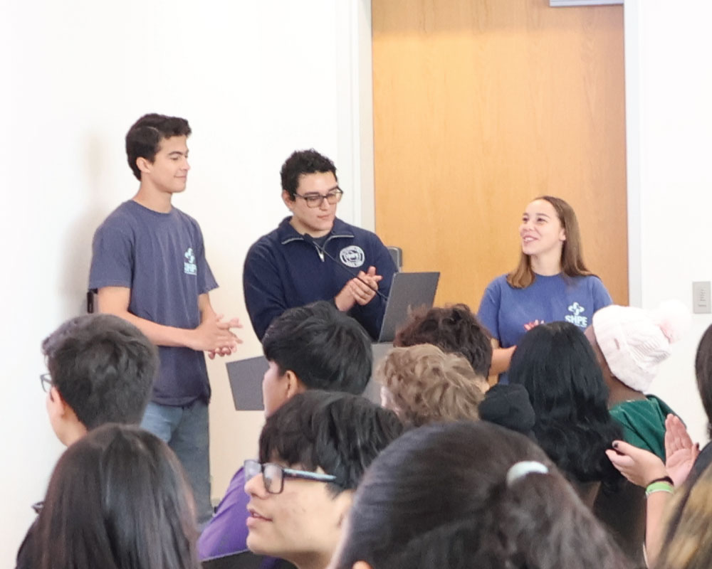 three undergraduate students presenting to a group of middle school students